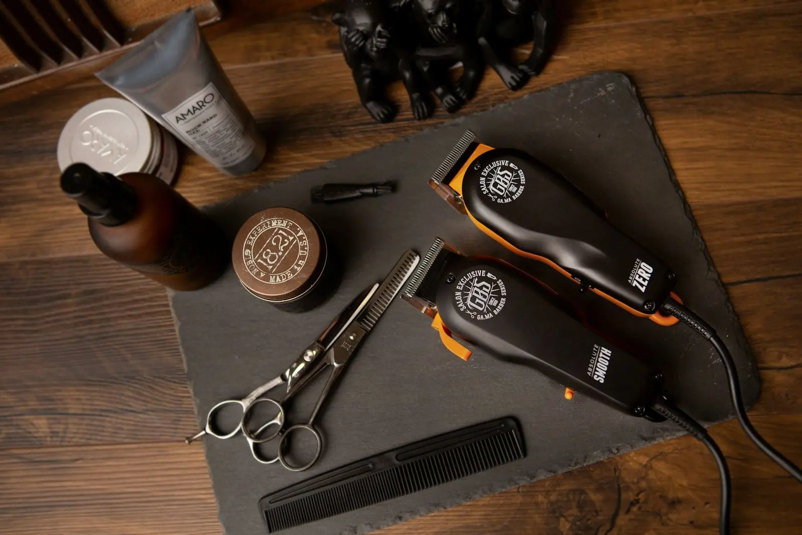 Clippers, shears, comb and pomade laid out on a slate board