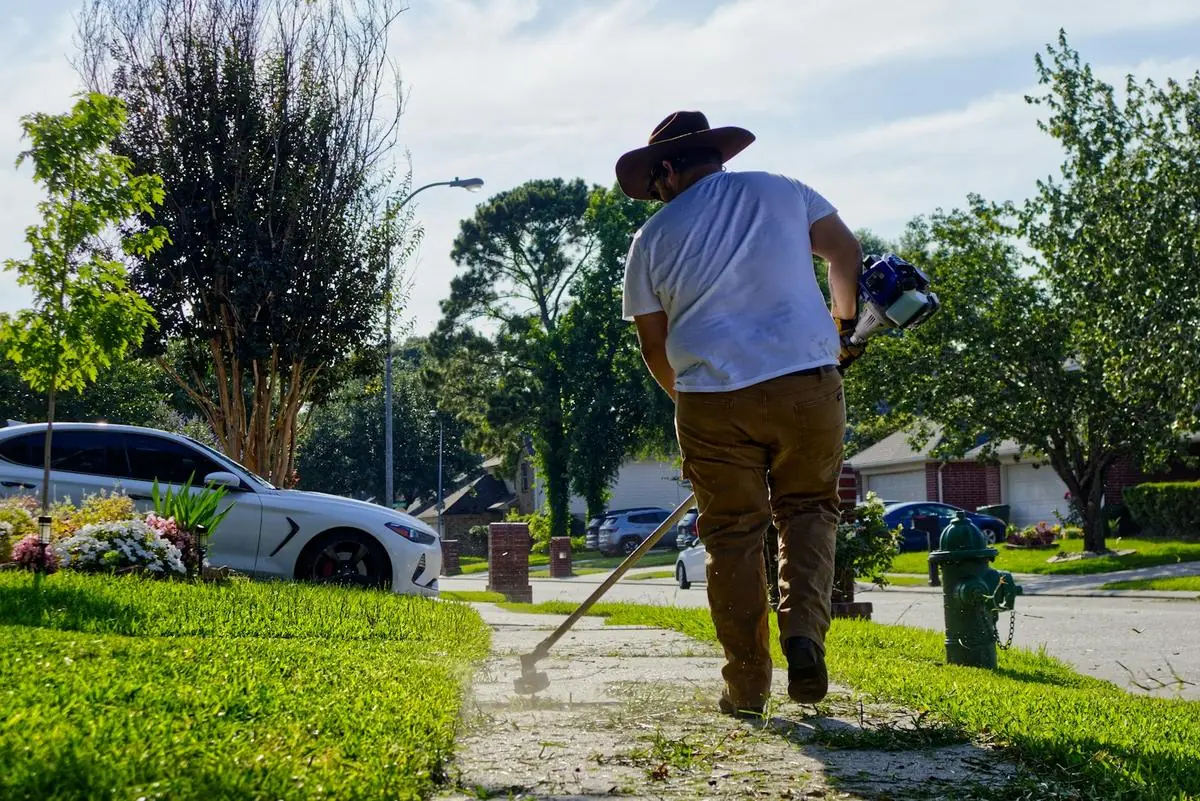 Crew member edging a sidewalk with a string trimmer