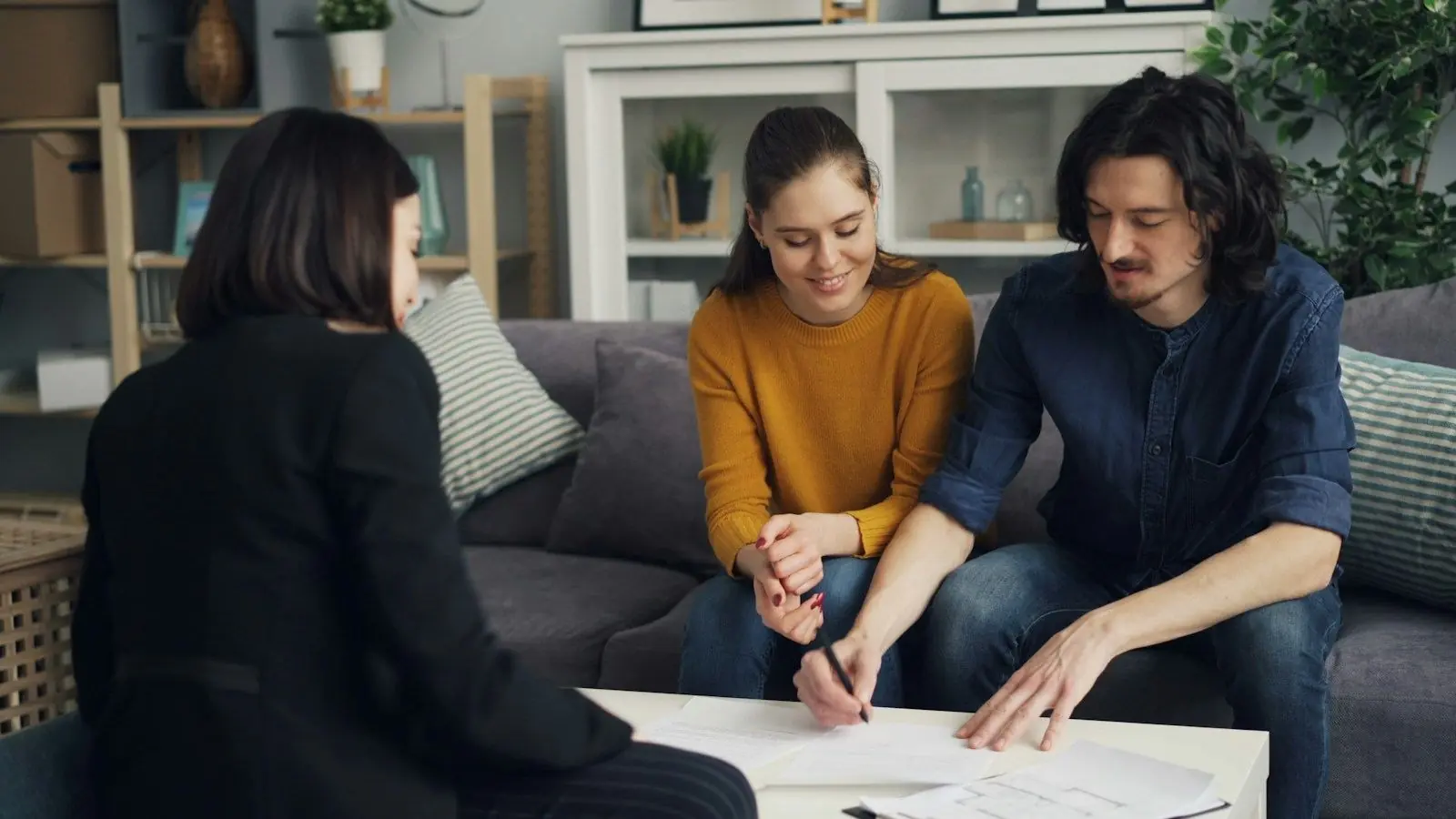 A couple reviewing and signing papers with an advisor at a coffee table