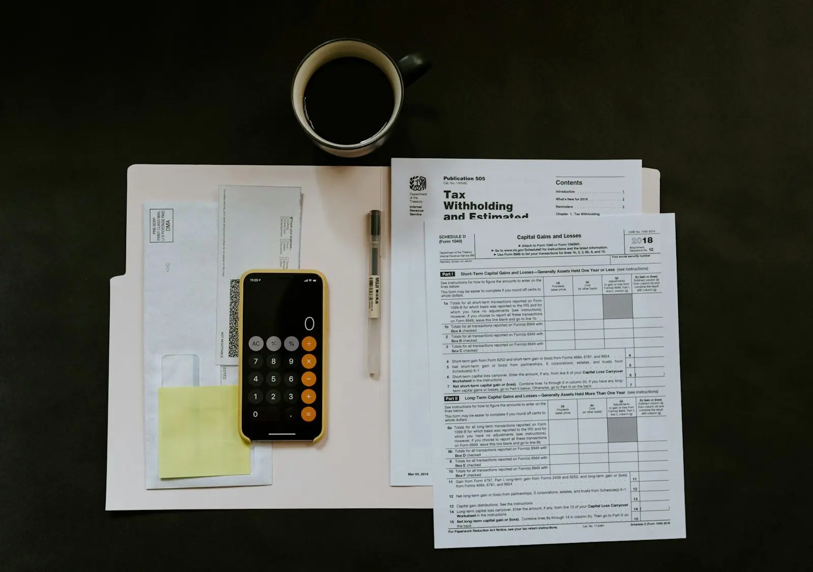 Tax forms, a phone calculator and a pen laid out on a desk next to a coffee cup